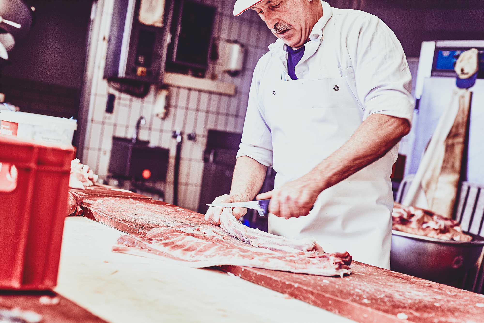 Ein Metzger bearbeitet mit einem Messer das Fleisch.